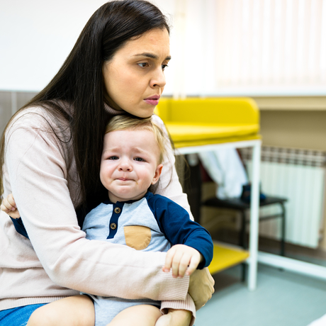 Un bébé pleure dans un bureau de médecin, assis sur les genoux de sa mère.