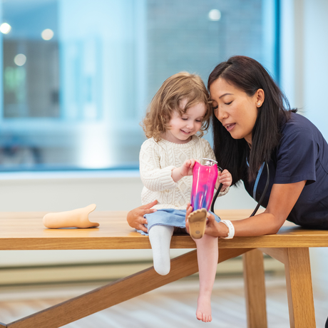 Une fillette avec une prothèse de jambe écoute attentivement sa médecin.