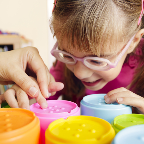 Une jeune fille atteinte d’un problème de vision joue avec des gobelets tactiles colorés dans le cadre d’une séance d’ergothérapie.