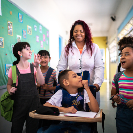 Une enseignante et ses élèves, dont un enfant ayant des besoins spéciaux, marchent dans un couloir.